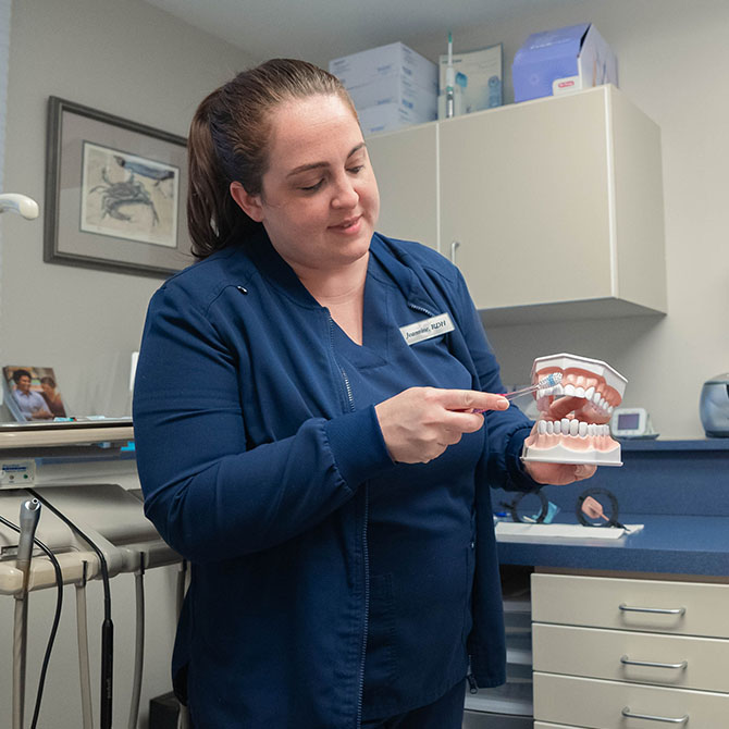A female dental staff member demonstrating how to properly brush teeth